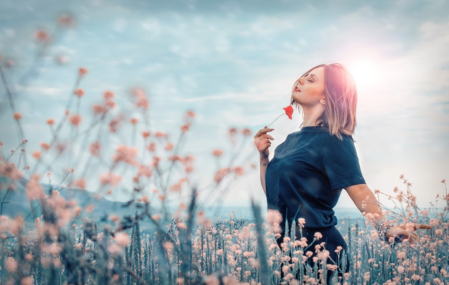 Praxis Dr. Schebitz – Frauenarzt – Eine Frau in einem blauen Hemd steht inmitten von rosa Blumen und hält eine rote Blume in der Hand